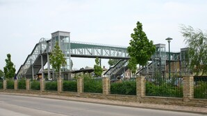 Eine moderne Brückenkonstruktion mit Metallträgern und Glasverkleidungen, umgeben von Steinmauern und Grünpflanzen.