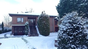 Um edifício de dois andares em tijolo, com um caminho de acesso coberto de neve e degraus que levam à entrada.