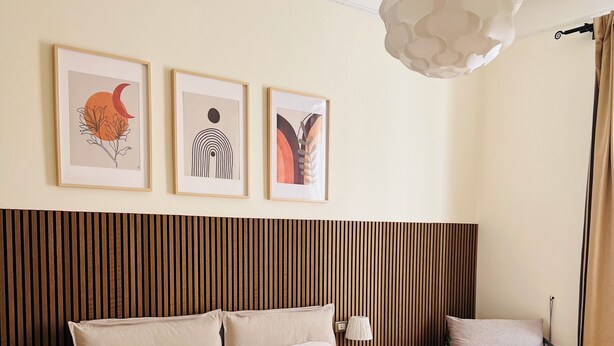 Un dormitorio con cama, mesitas de noche, una silla y cuadros en la pared.