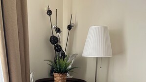 Una habitación con un barril de madera con la etiqueta 'SANTI 1843', un sofá gris, una lámpara de pie y una planta en maceta con detalles decorativos.