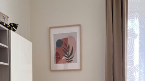 Una habitación minimalista con una obra de arte abstracta enmarcada, una mesita con una planta y un armario blanco.