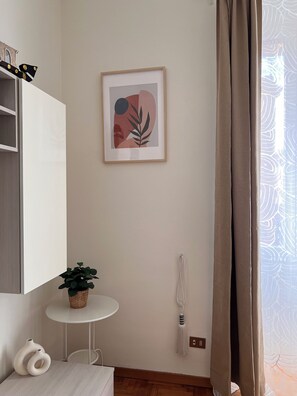 Ein schlichter Raum mit einem gerahmten abstrakten Kunstwerk, einem kleinen Tisch mit einer Pflanze und einem weißen Schrank.