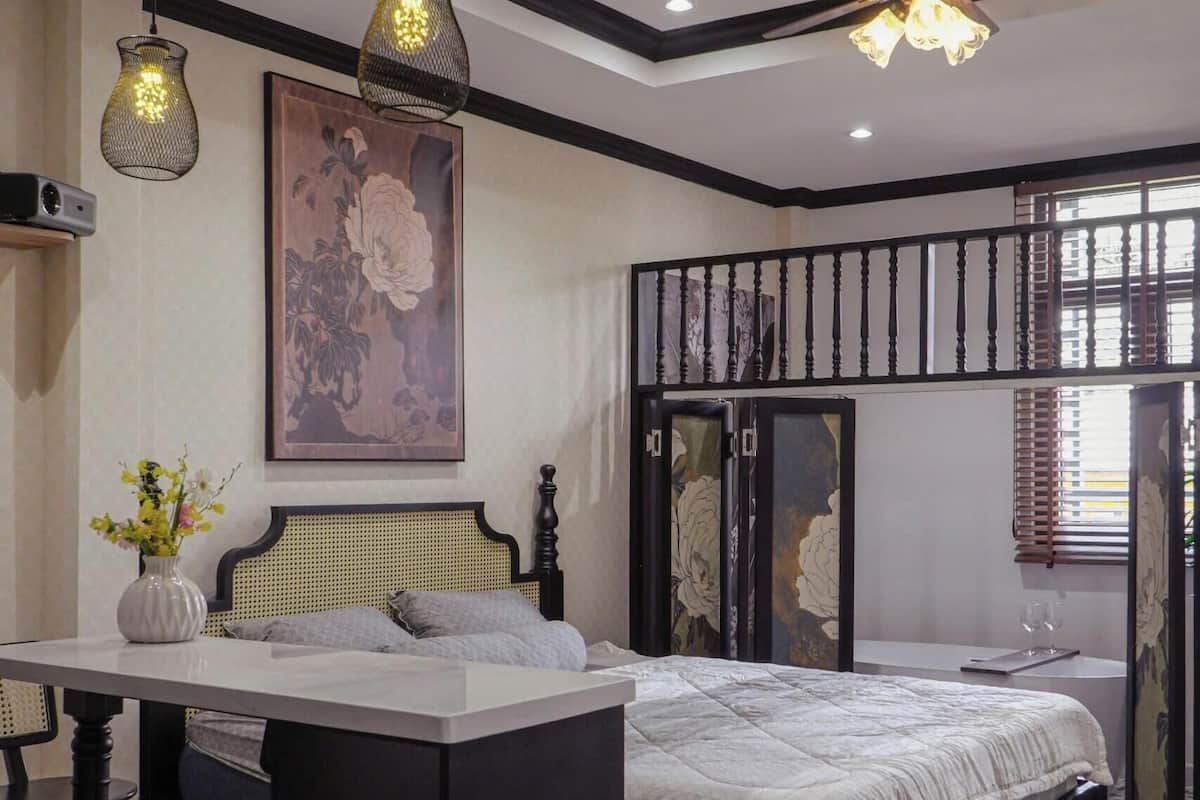 Un dormitorio con cama, escritorio, silla, ventilador de techo y un cuadro en la pared.