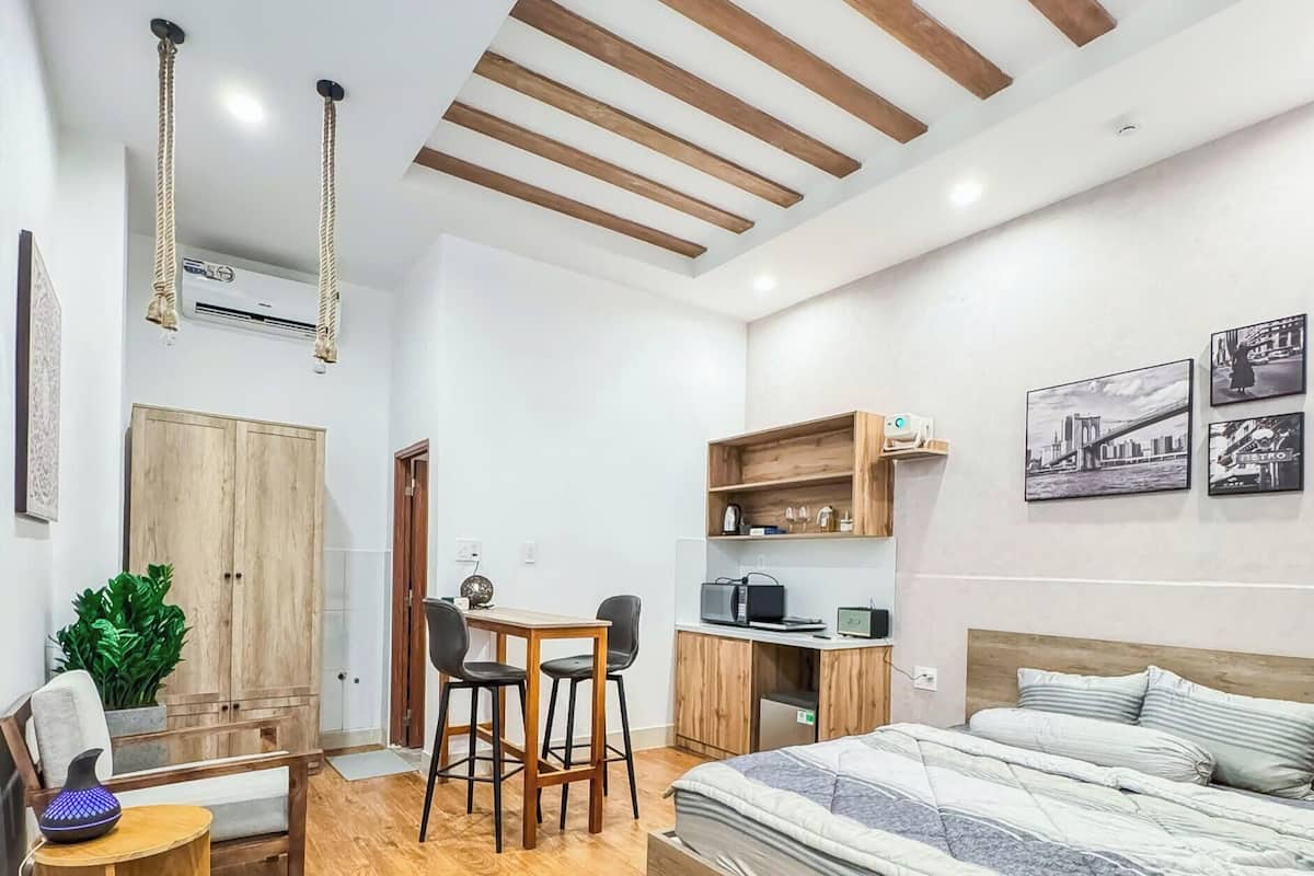 Un dormitorio moderno con suelo de madera, una cama, un escritorio con sillas, un armario y una kitchenette.