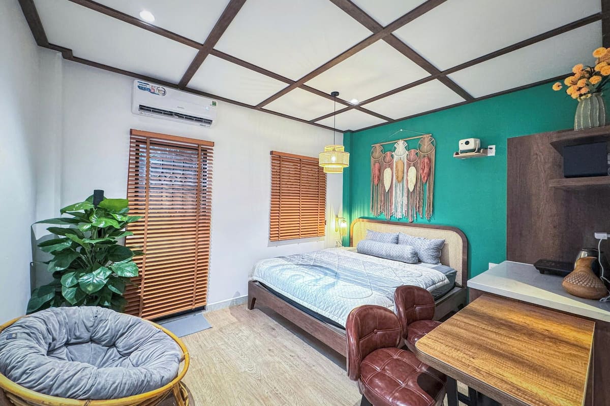 Un dormitorio con cama, escritorio, silla, lámpara colgante, aire acondicionado de pared y planta en maceta.