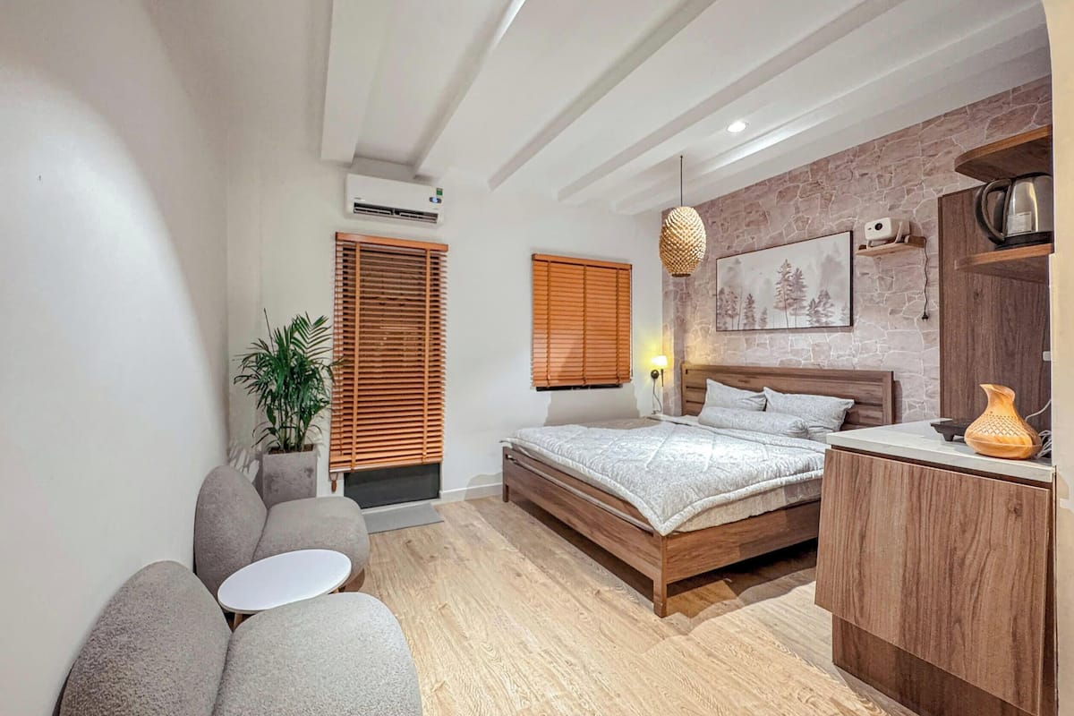 Un dormitorio con una cama, una mesita, un sofá, una planta en maceta y un armario de madera.