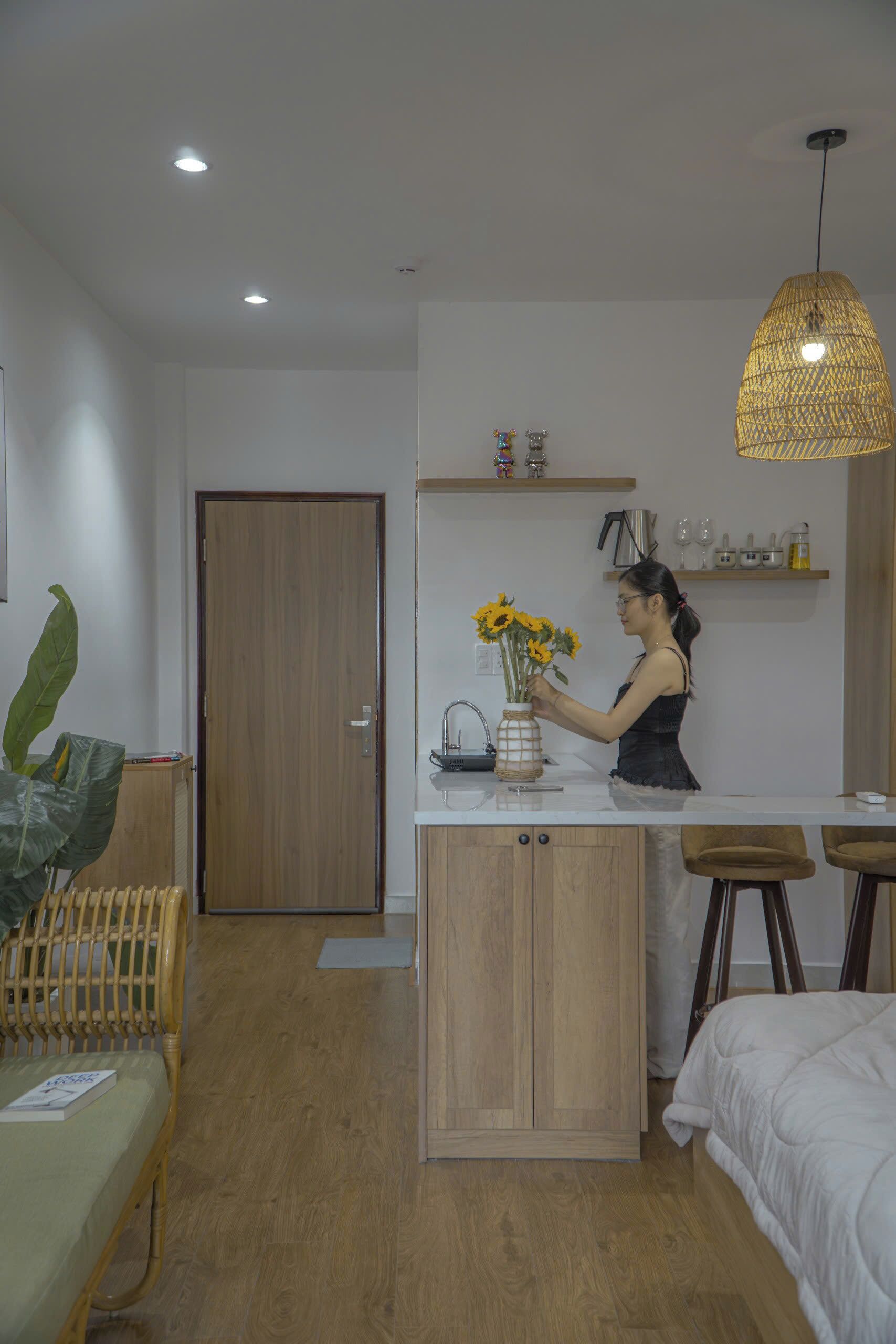 A modern kitchen with a wooden cabinet, a hanging light fixture, and a person arranging flowers on the counter.