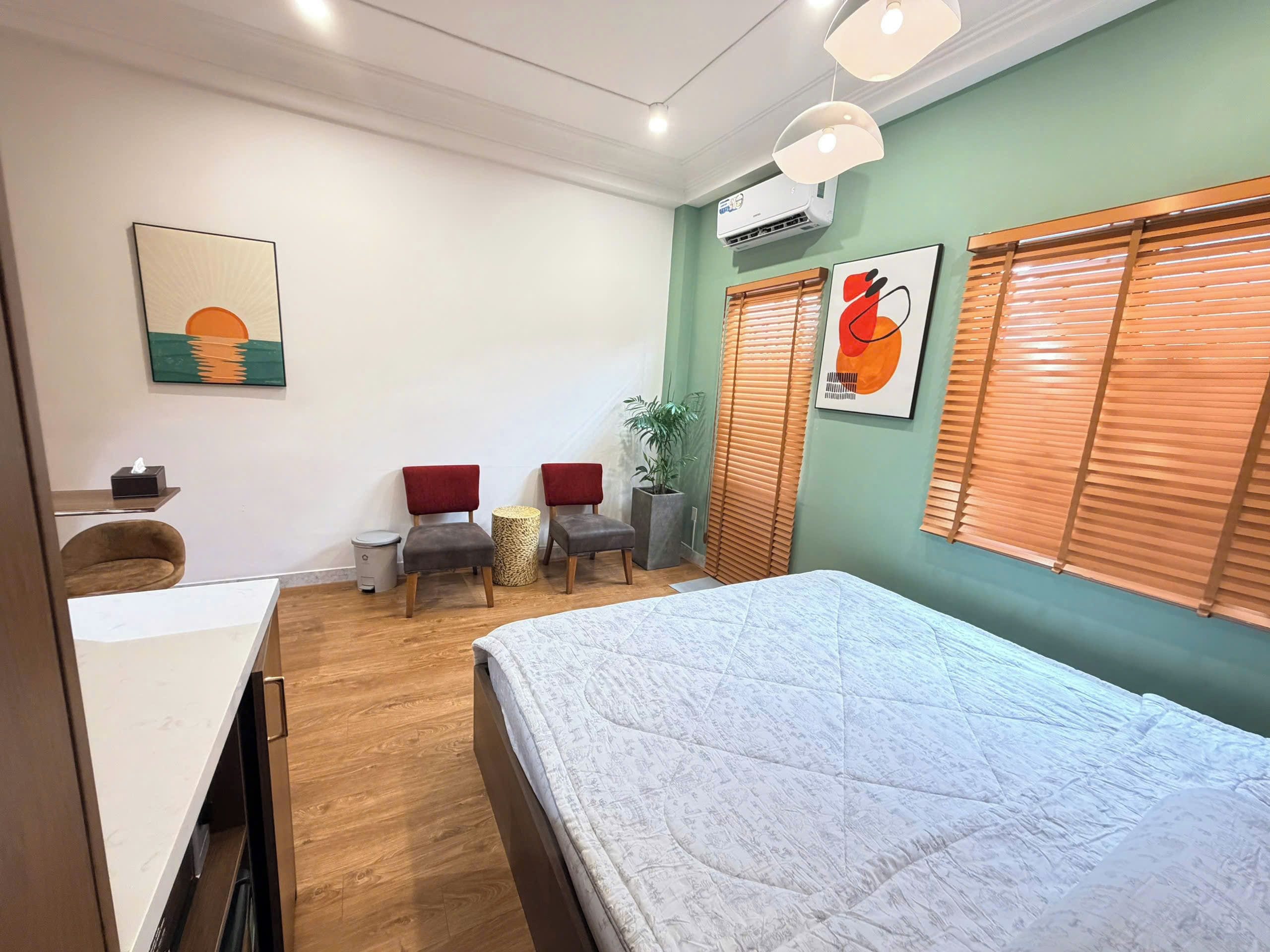 A hotel room with a bed, two chairs, a small table, and a potted plant.