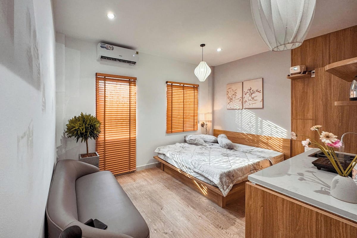Un dormitorio con cama, mesita de noche, banco y una planta en maceta.