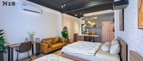A hotel room with a bed, a desk, a sofa, a kitchenette, and a large mirror.