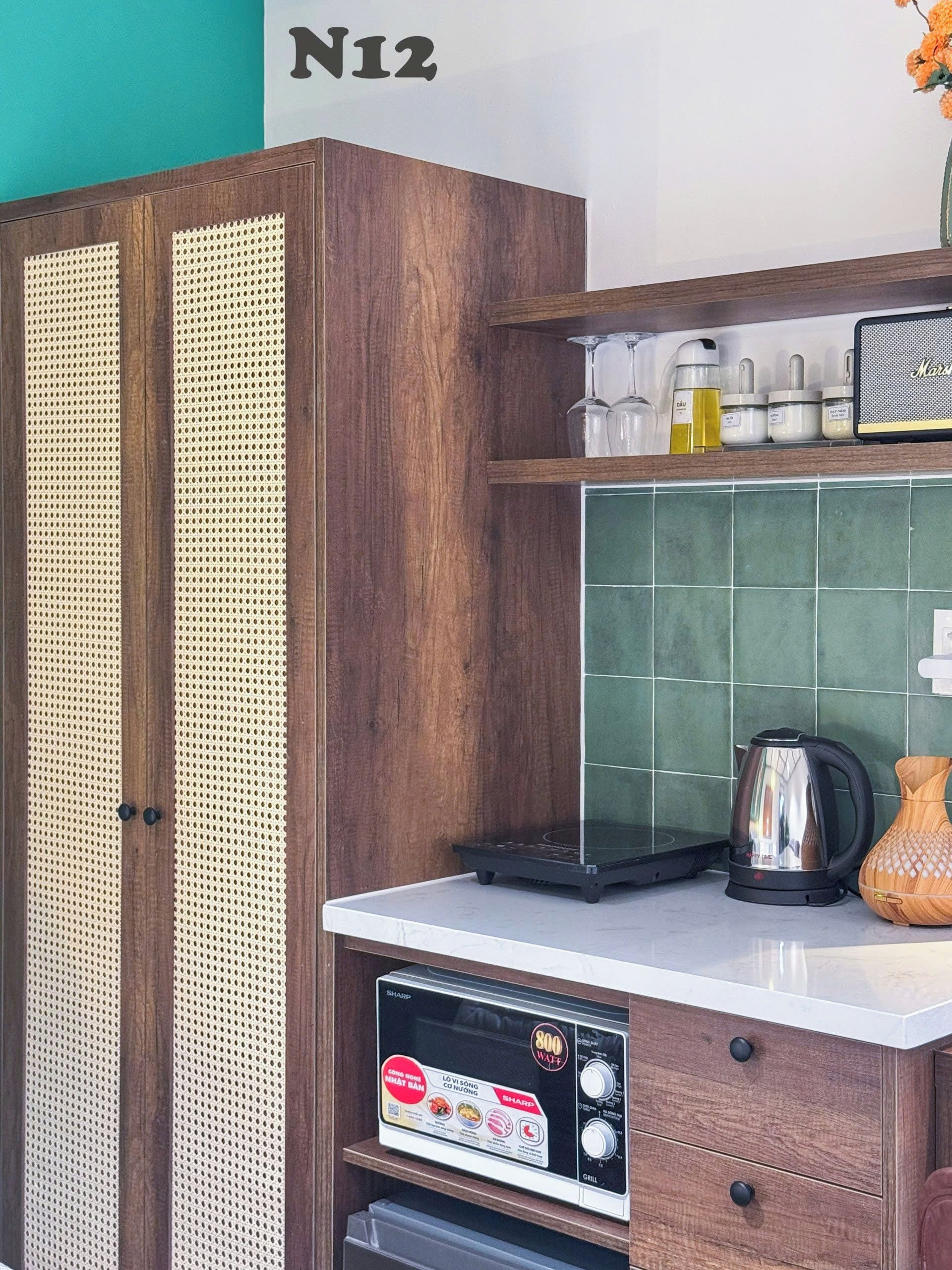 A kitchen with a microwave, kettle, and a cabinet with a perforated door.
