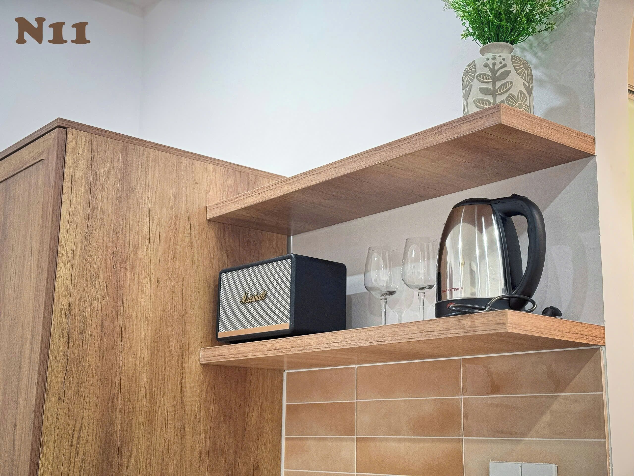 A kitchen with a wooden cabinet, a coffee maker, and a vase with green plants on a shelf.