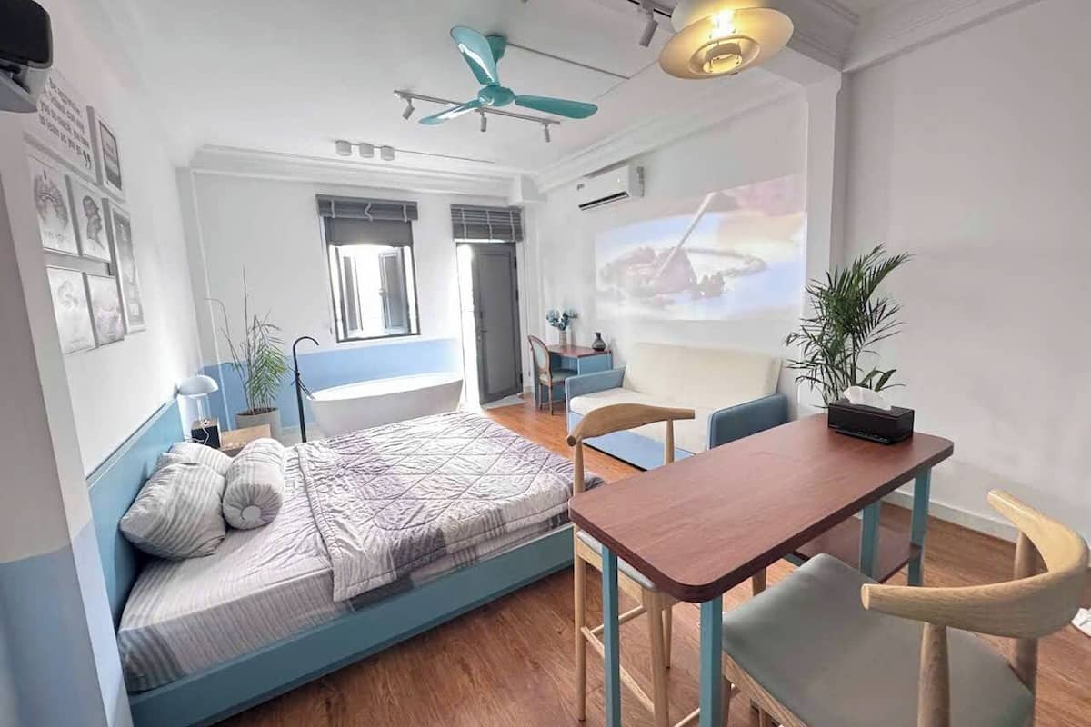 Una habitación moderna con cama, escritorio, sillas, ventilador de techo y pantalla para proyector.