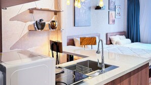 Une cuisine moderne équipée d’un lave-vaisselle encastré, d’un évier et d’un plan de travail. On aperçoit des luminaires suspendus et, au fond, un lit avec une tête de lit.