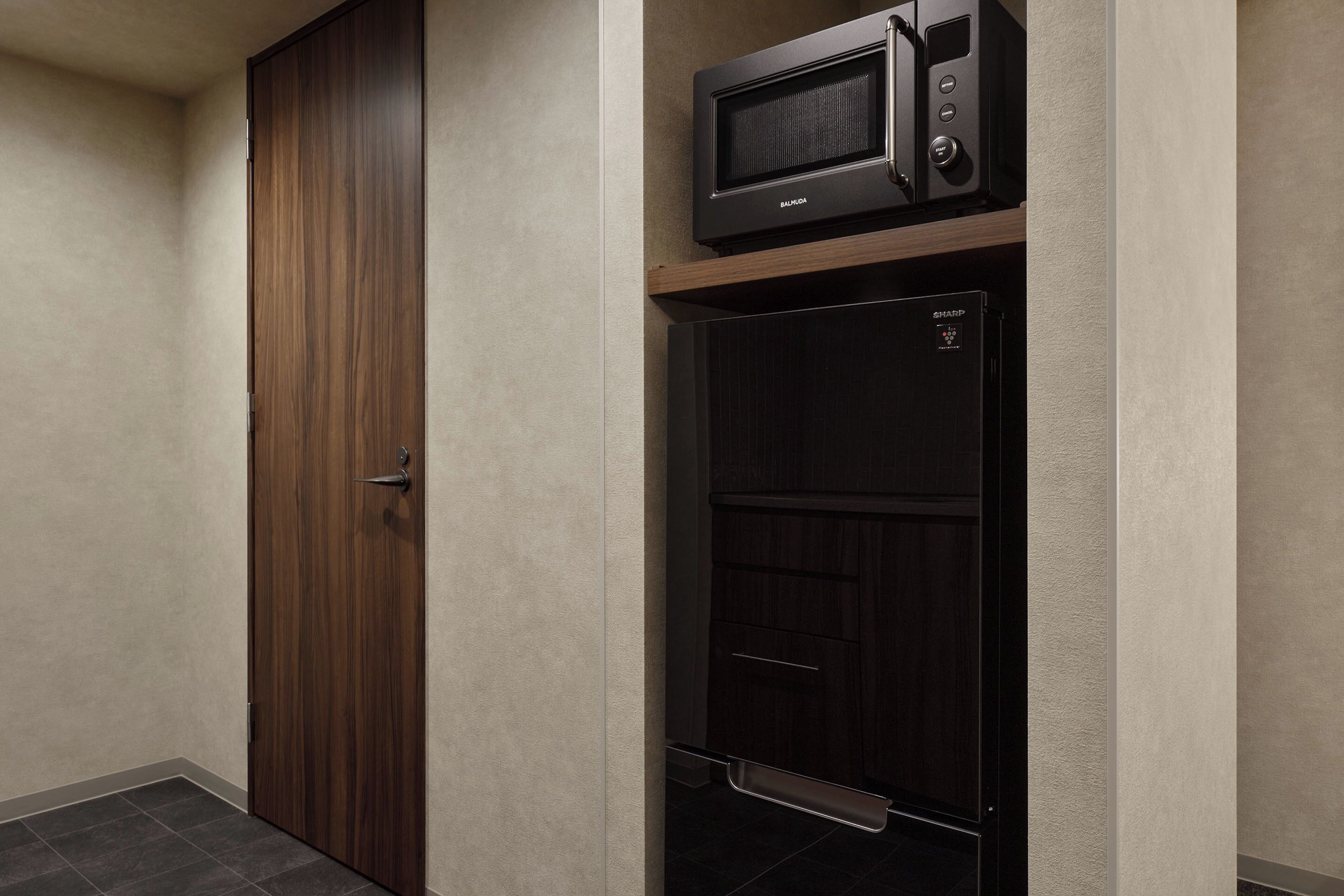 Una stanza con una porta in legno, un forno a microonde e un mobiletto nero con un pannello di controllo.