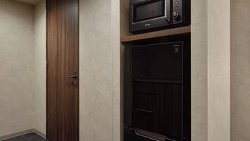 Una stanza con una porta in legno, un forno a microonde e un mobiletto nero con un pannello di controllo.