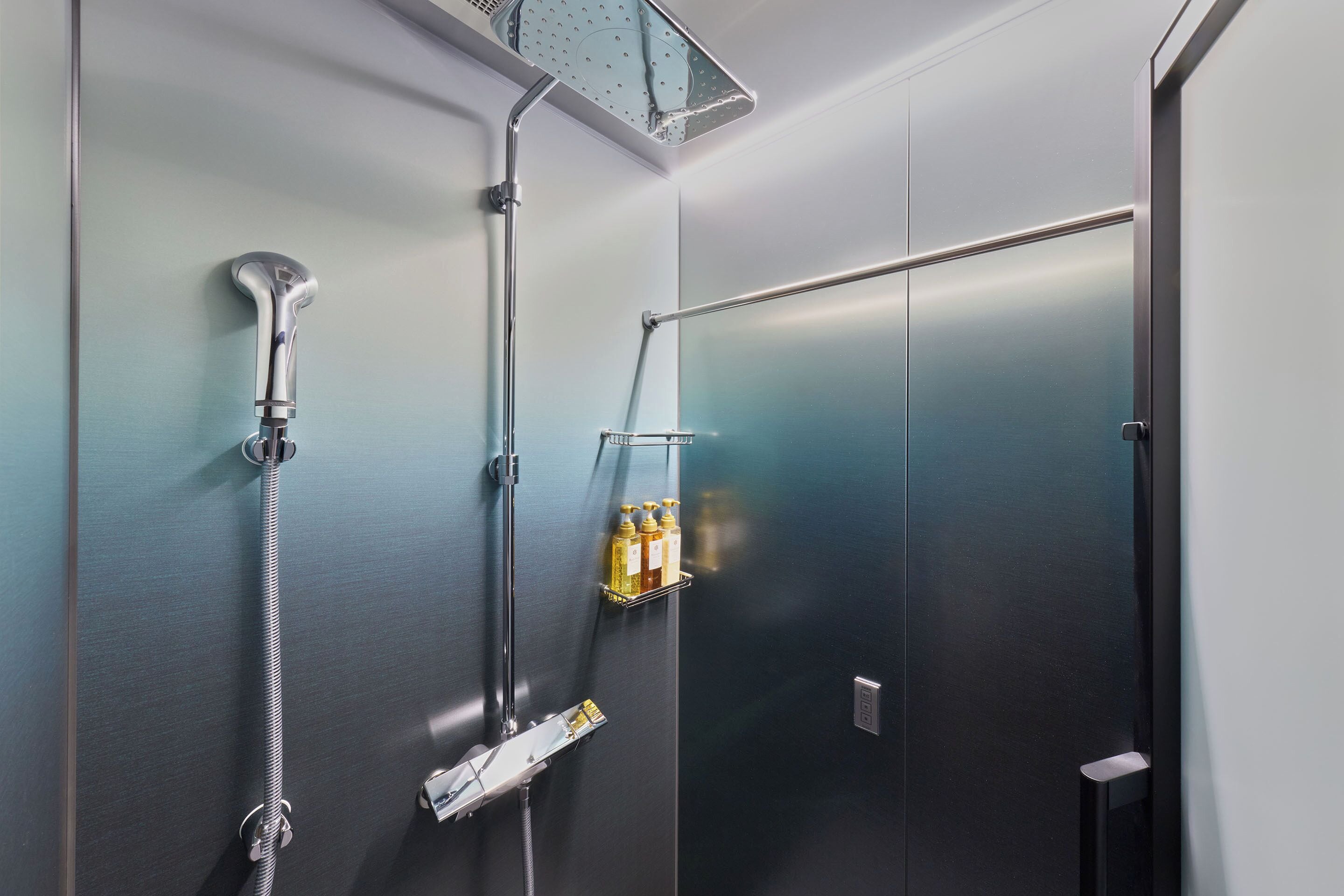 A modern bathroom with a shower, a hand dryer, and a soap dispenser on a wall-mounted rack.