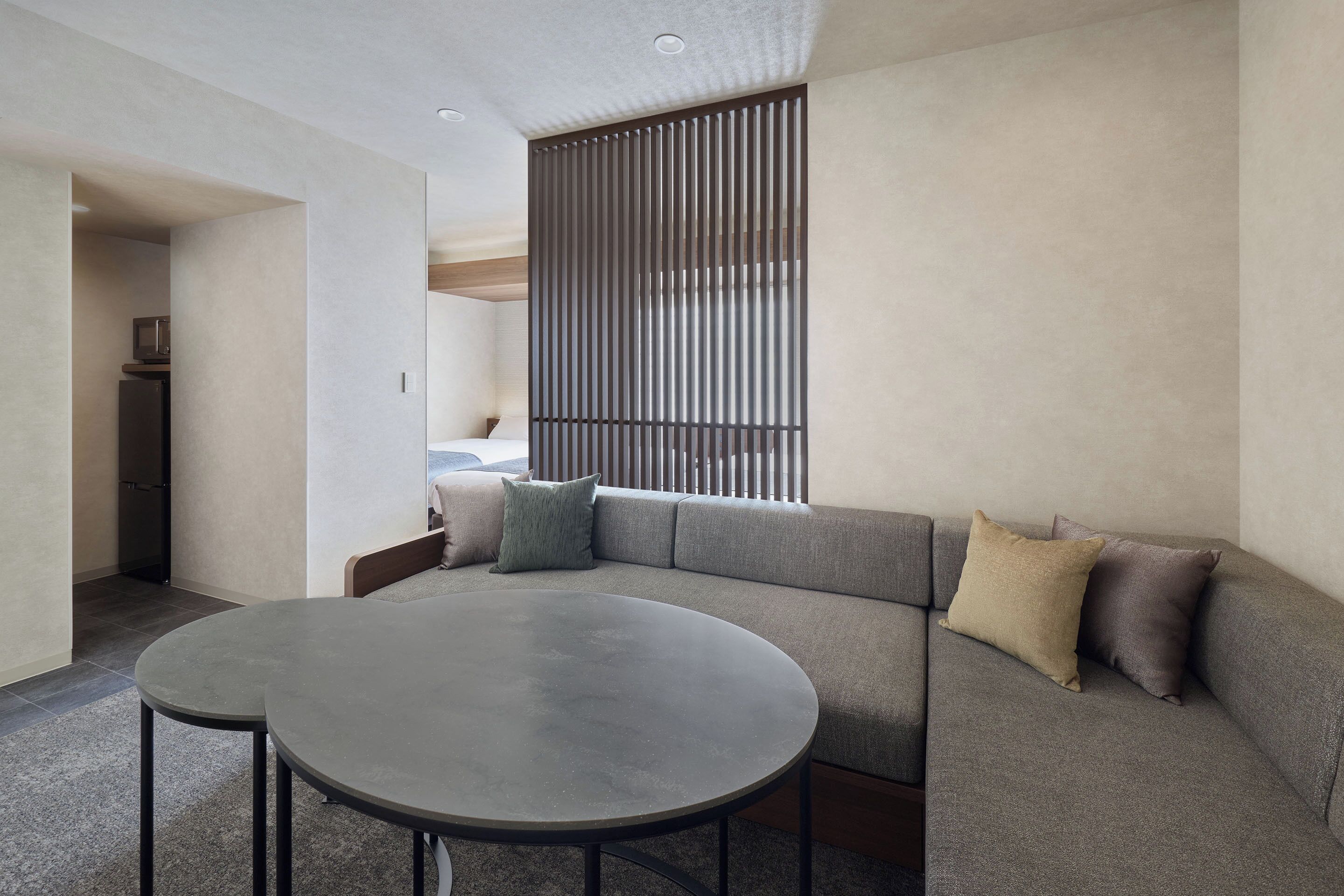 A modern living room with a sectional sofa, a round table, and a kitchen area visible through an open doorway.
