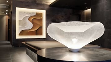 Un intérieur moderne avec un luminaire original placé sur une plateforme circulaire, un banc et une œuvre d’art abstraite fixée au mur.