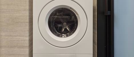 A front view of a white washing machine with a circular door, mounted on a wall with a textured surface.
