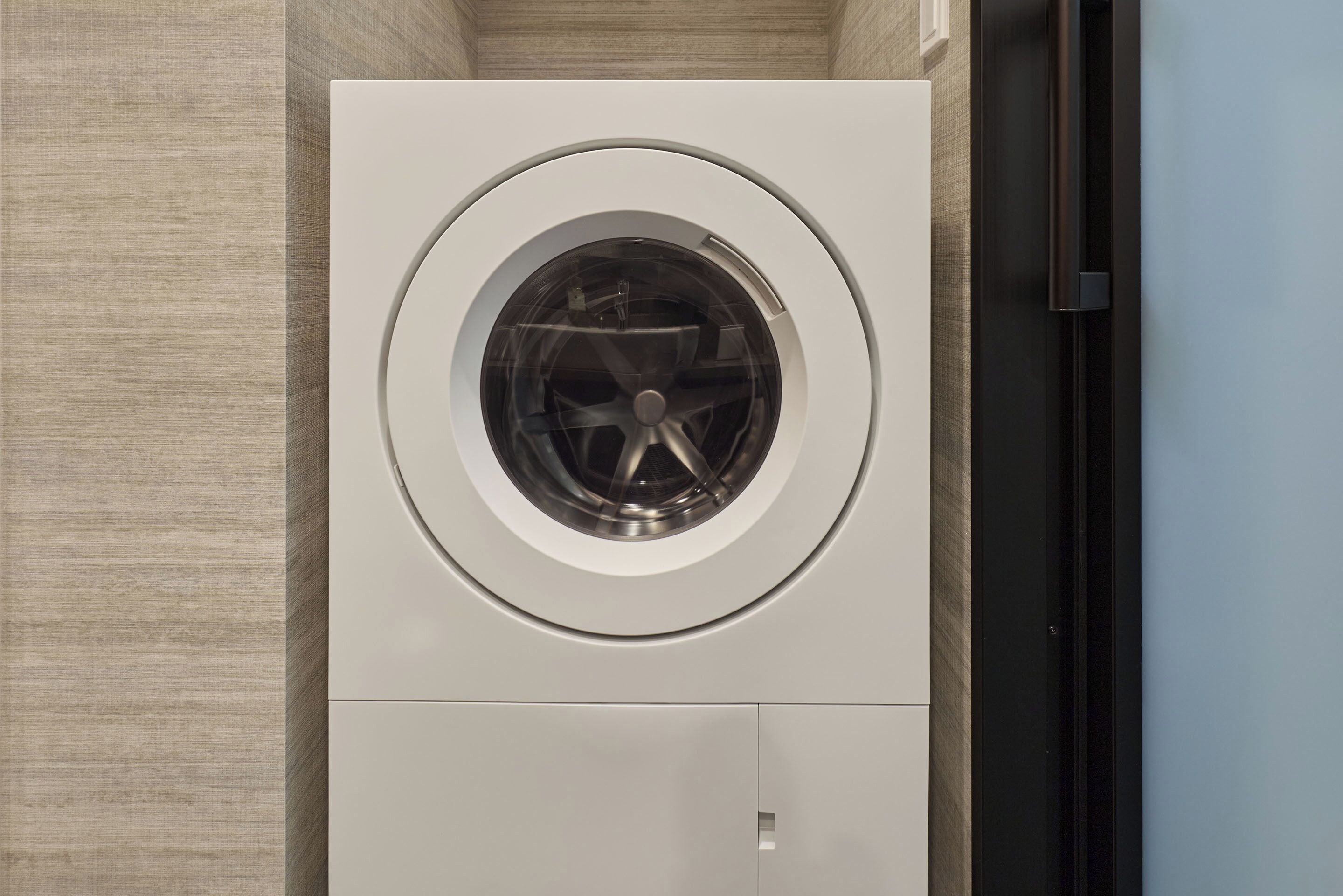 A front view of a wall-mounted washing machine with a circular door, set against a textured wall.