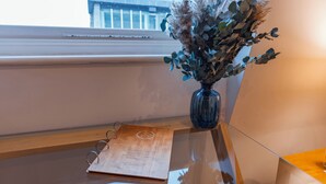 A wooden desk with a glass top, a blue vase with dried plants, and a wooden folder with text. - Cannon Street Serviced Apartments (London)