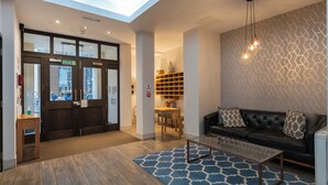 A hotel lobby with a reception desk, a black leather sofa, a glass coffee table, a patterned rug, and a geometric wall design. - Cannon Street Serviced Apartments (London)