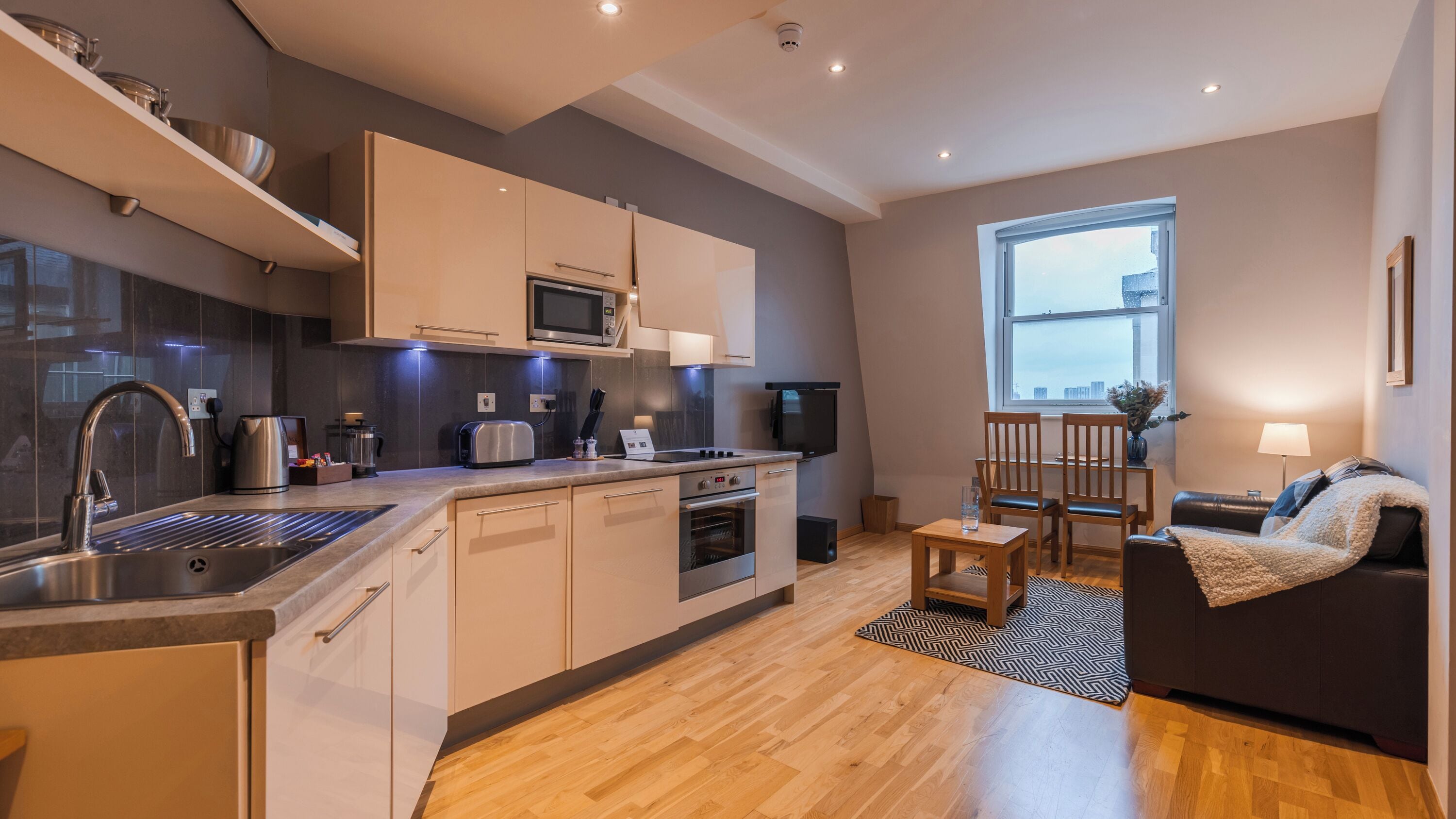 A modern kitchen with built-in appliances, a dining area with a sofa and table, and a large window providing natural light.