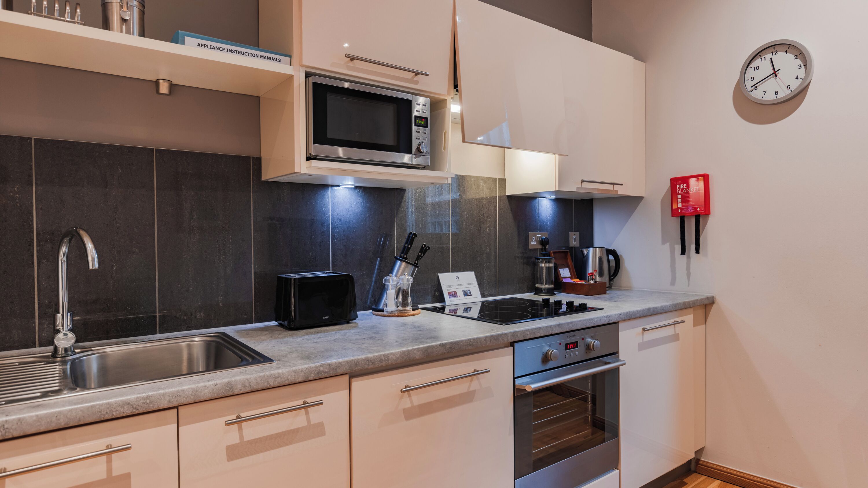 A modern kitchen with a microwave, toaster, stove, sink, and a clock on the wall.
