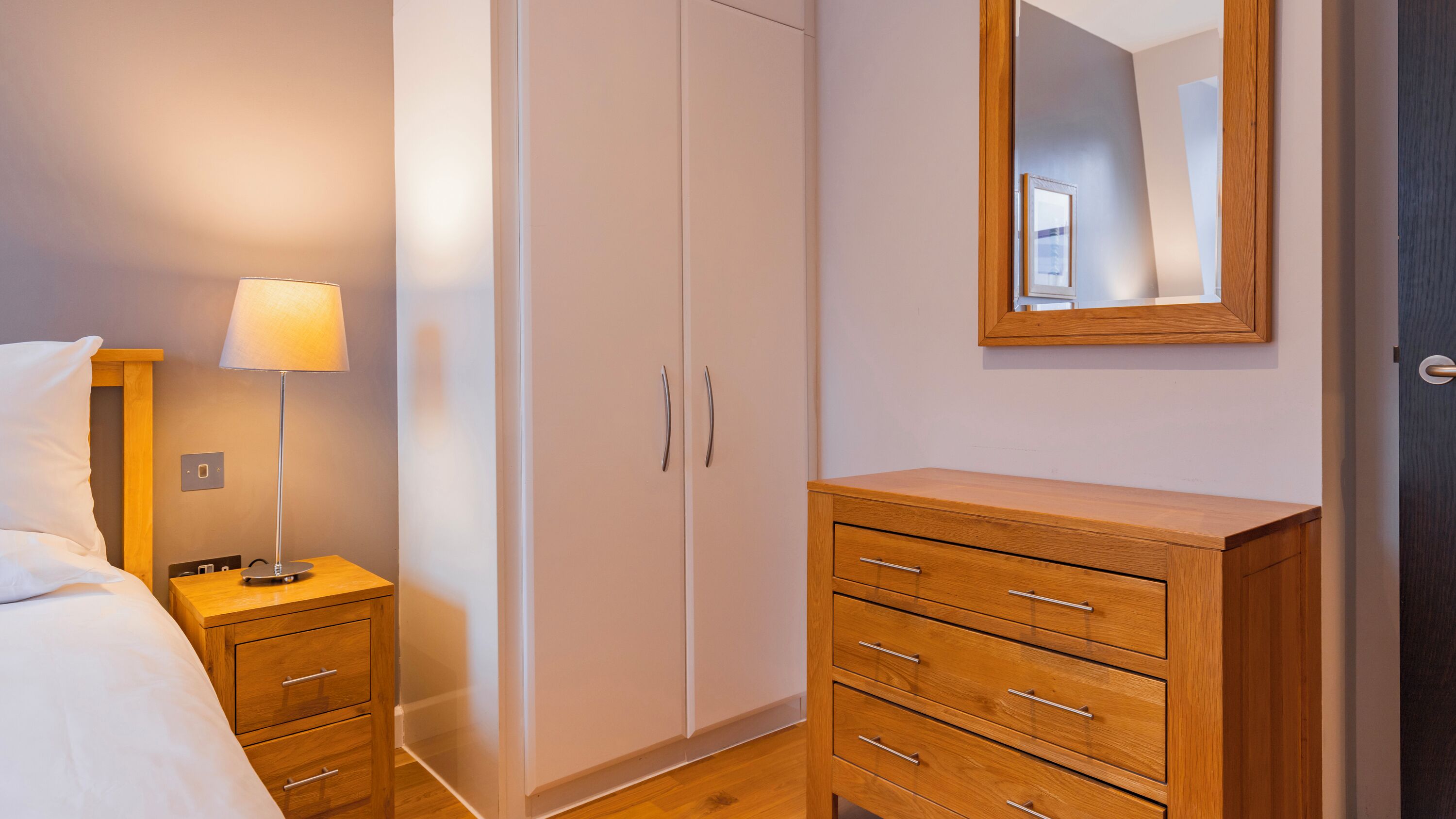 A bedroom with a bed, bedside table, lamp, wardrobe, and a mirror.