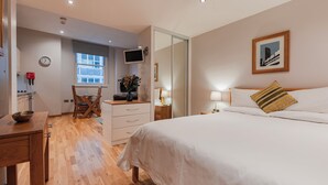 A bedroom with a bed, bedside table, lamp, and a painting on the wall. - Cannon Street Serviced Apartments (London)