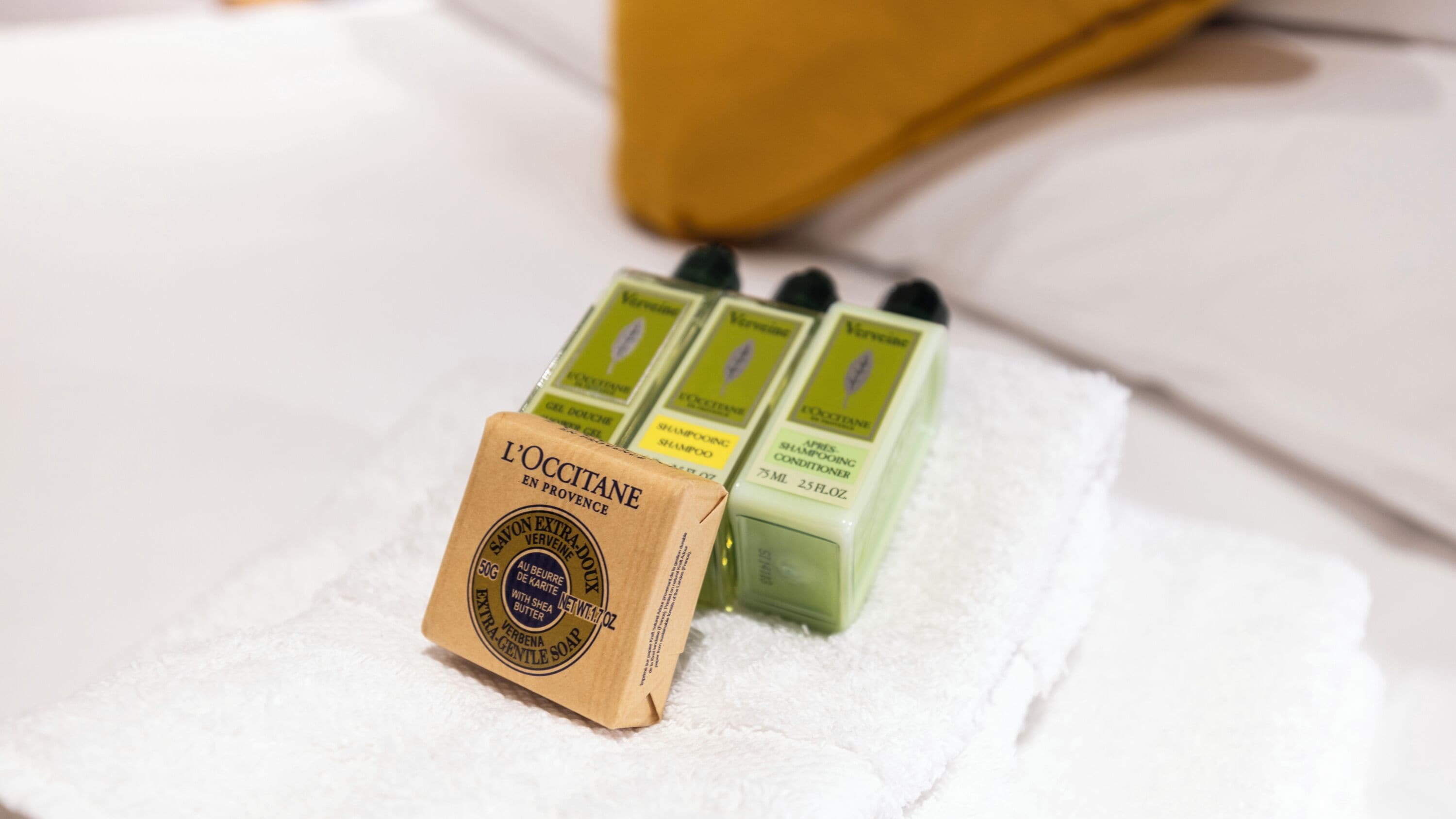 Eine Packung L'OCCITANE Seife und drei Shampooflaschen auf einem weißen Handtuch.