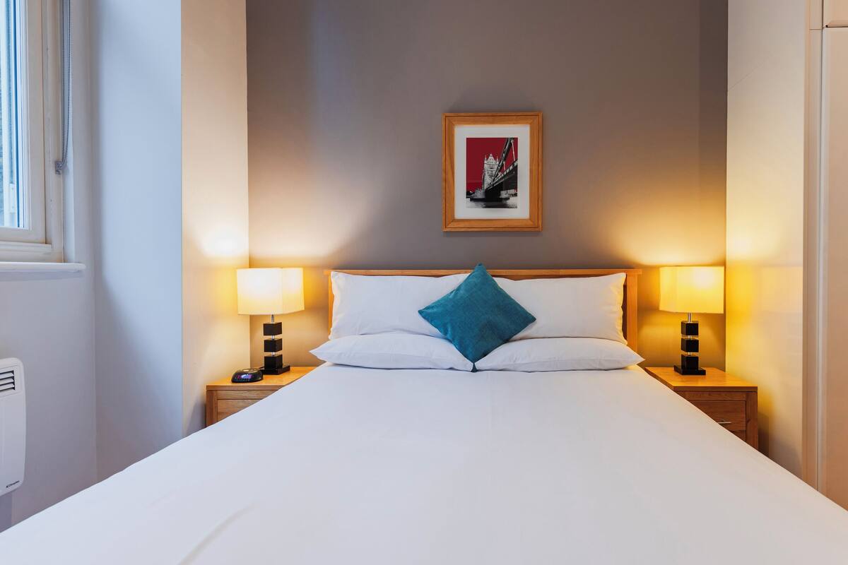 A hotel room with a bed, two bedside lamps, a framed picture on the wall, and a wardrobe.