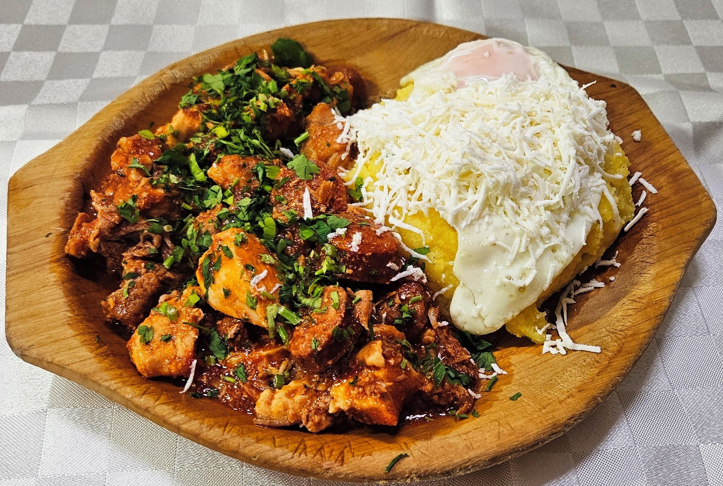 Une assiette en bois contenant un repas composé d’un œuf frit, d’une tranche de fromage et d’un plat de viande agrémenté d’herbes.