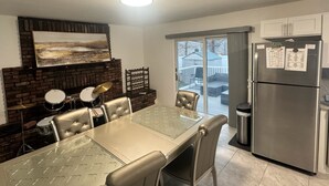 Una cocina con una mesa de comedor, sillas, un refrigerador y vistas al exterior a través de un ventanal.