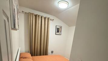 A bedroom with a bed, curtains, a ceiling light, a wall-mounted picture, and a wooden floor.