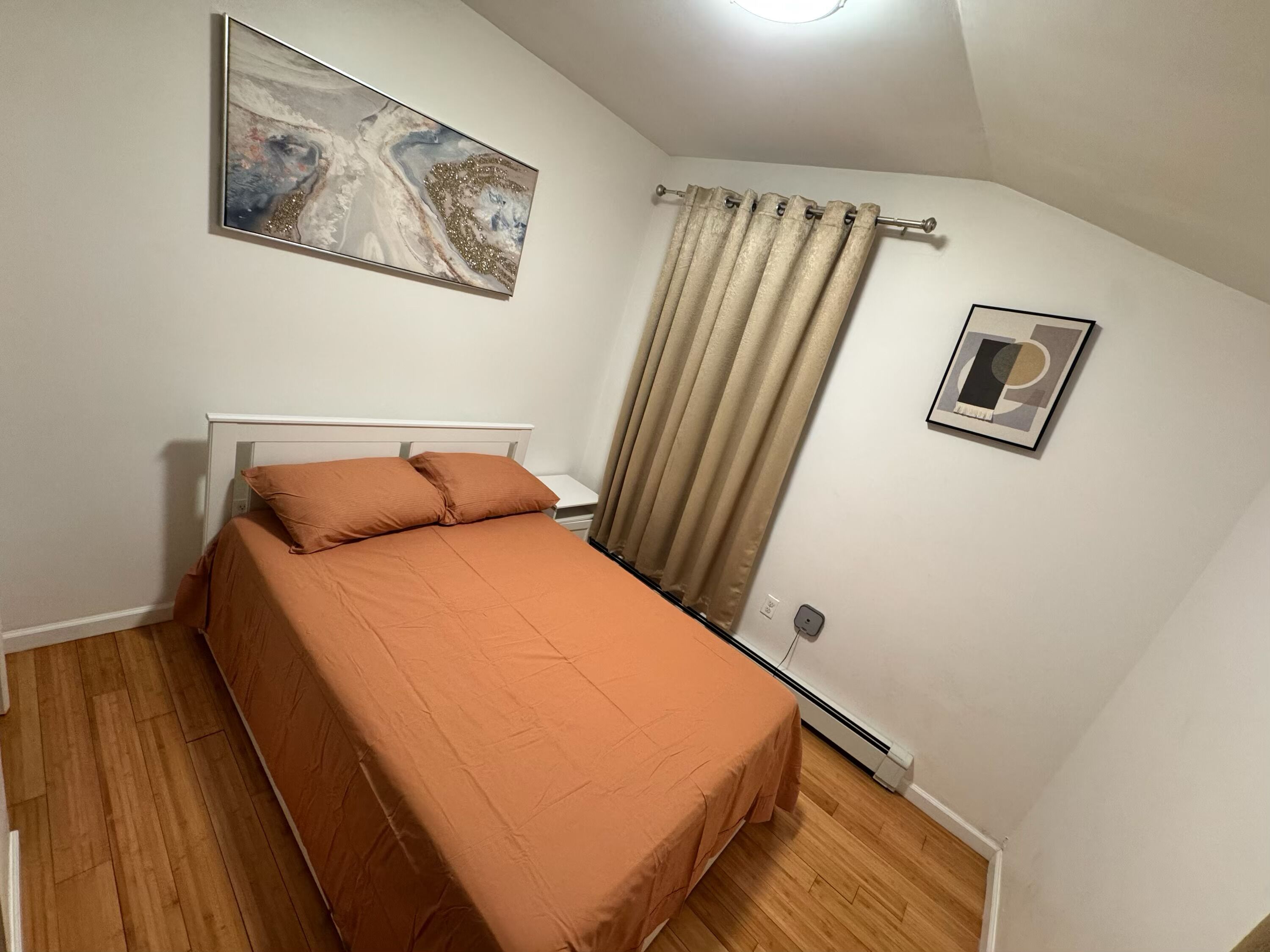 A bedroom with a bed, a painting, a curtain, and a picture on the wall.