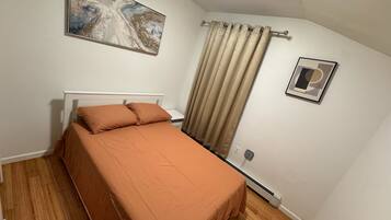 A bedroom with a bed, a painting, a curtain, and a picture on the wall.