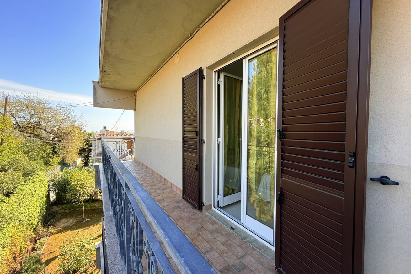 Een balkon met uitzicht op een tuin en een gebouw aan de overkant van de straat.