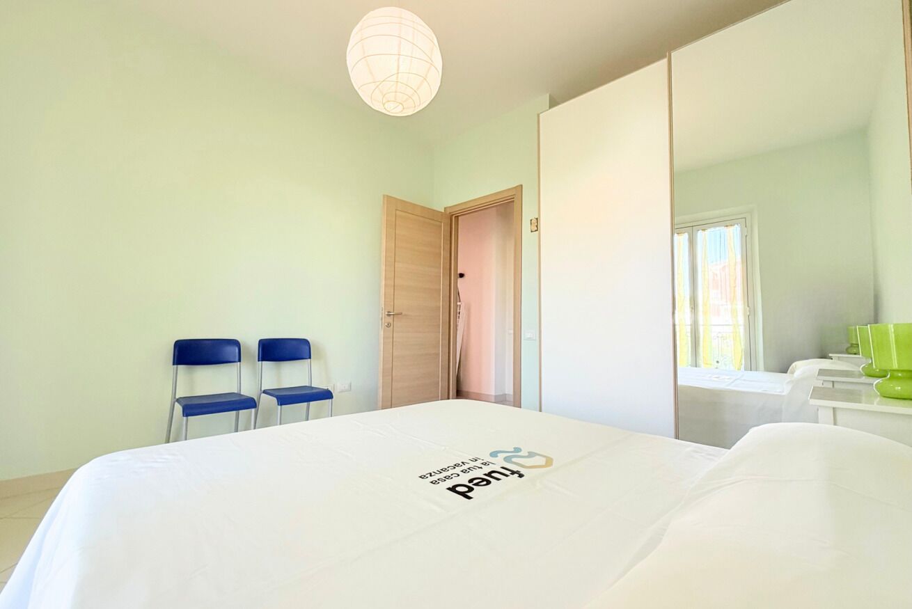 Een hotelkamer met een bed, twee stoelen, een kledingkast, een spiegel en een raam.