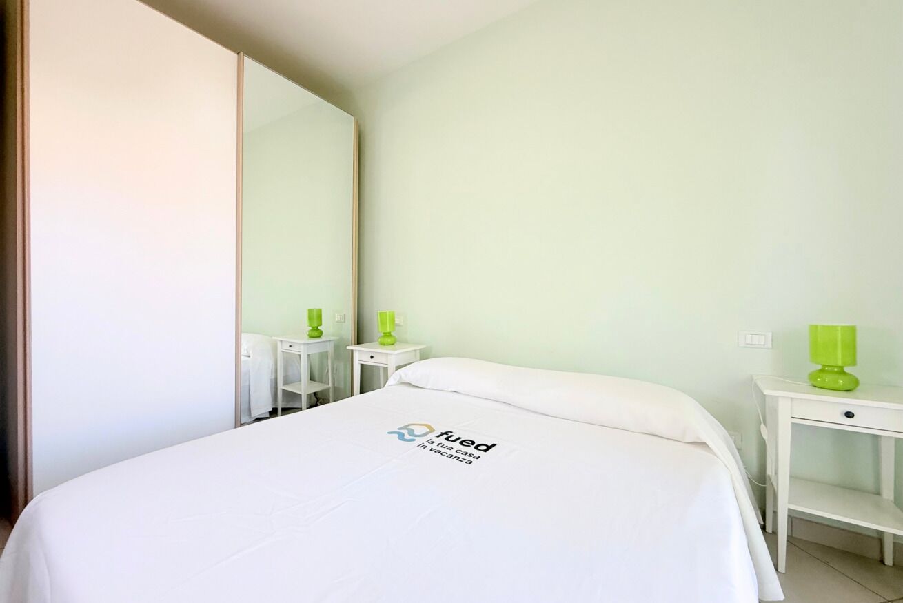 A hotel room with a bed, a nightstand, a mirror, and a green lamp.