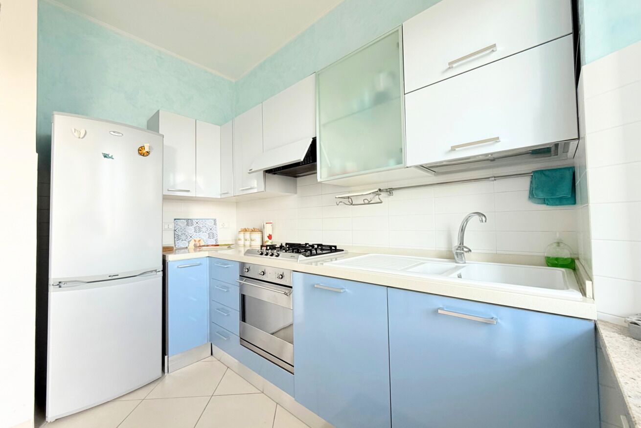 Een keuken met witte kastjes, een blauw aanrecht, een fornuis en een spoelbak.
