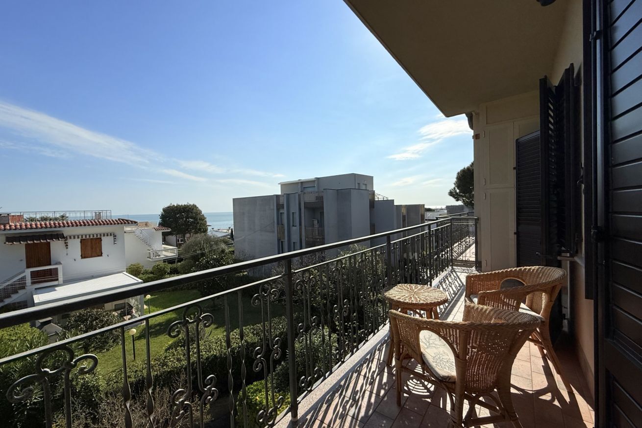Een balkon met rieten meubilair, uitzicht op gebouwen en een heldere lucht.