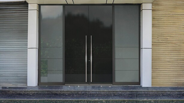 Une entrée moderne, avec une porte en verre, un volet métallique et un socle en béton.