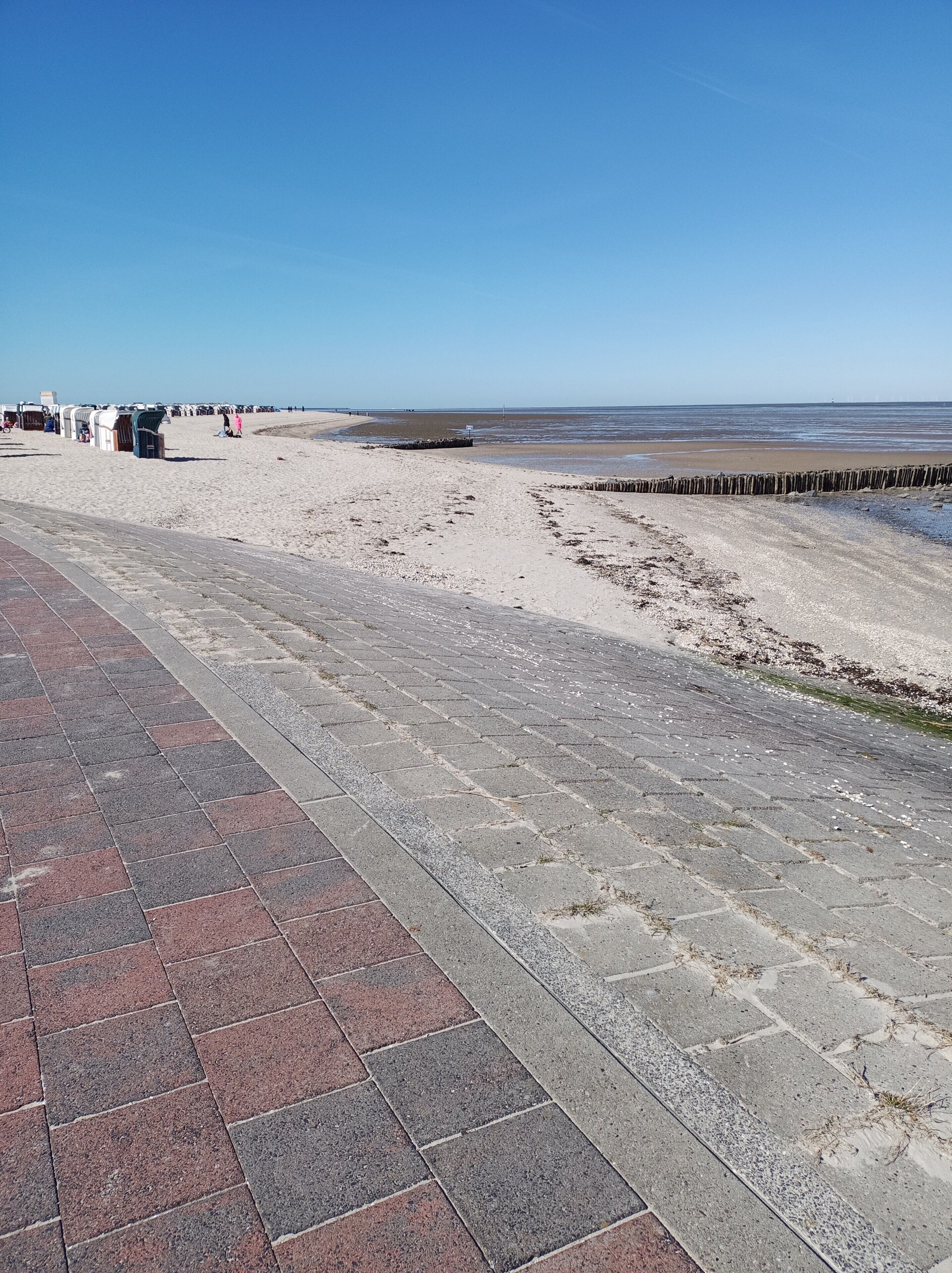Un chemin pavé mène à une plage, et une barrière en bois en bloque l’accès.