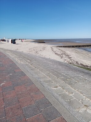 Ein gepflasterter Weg führt zu einem Strand mit einer Holzbarriere.