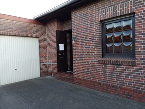 Um edifício de tijolos com uma porta de garagem branca, uma porta preta e uma janela com grade.