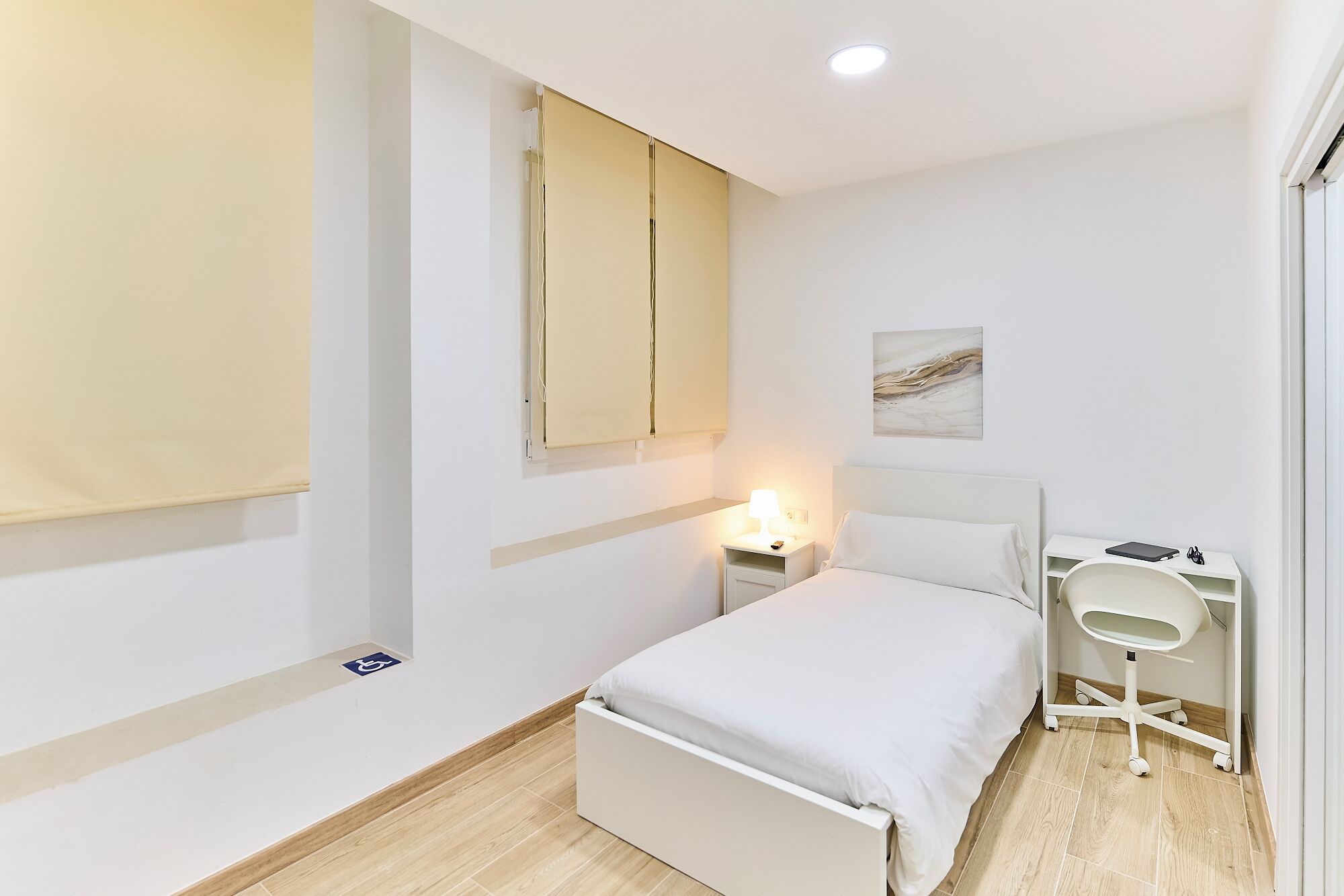 Ein schlicht eingerichtetes Schlafzimmer mit Bett, Nachttisch und kleinem Schreibtisch mit Stuhl.