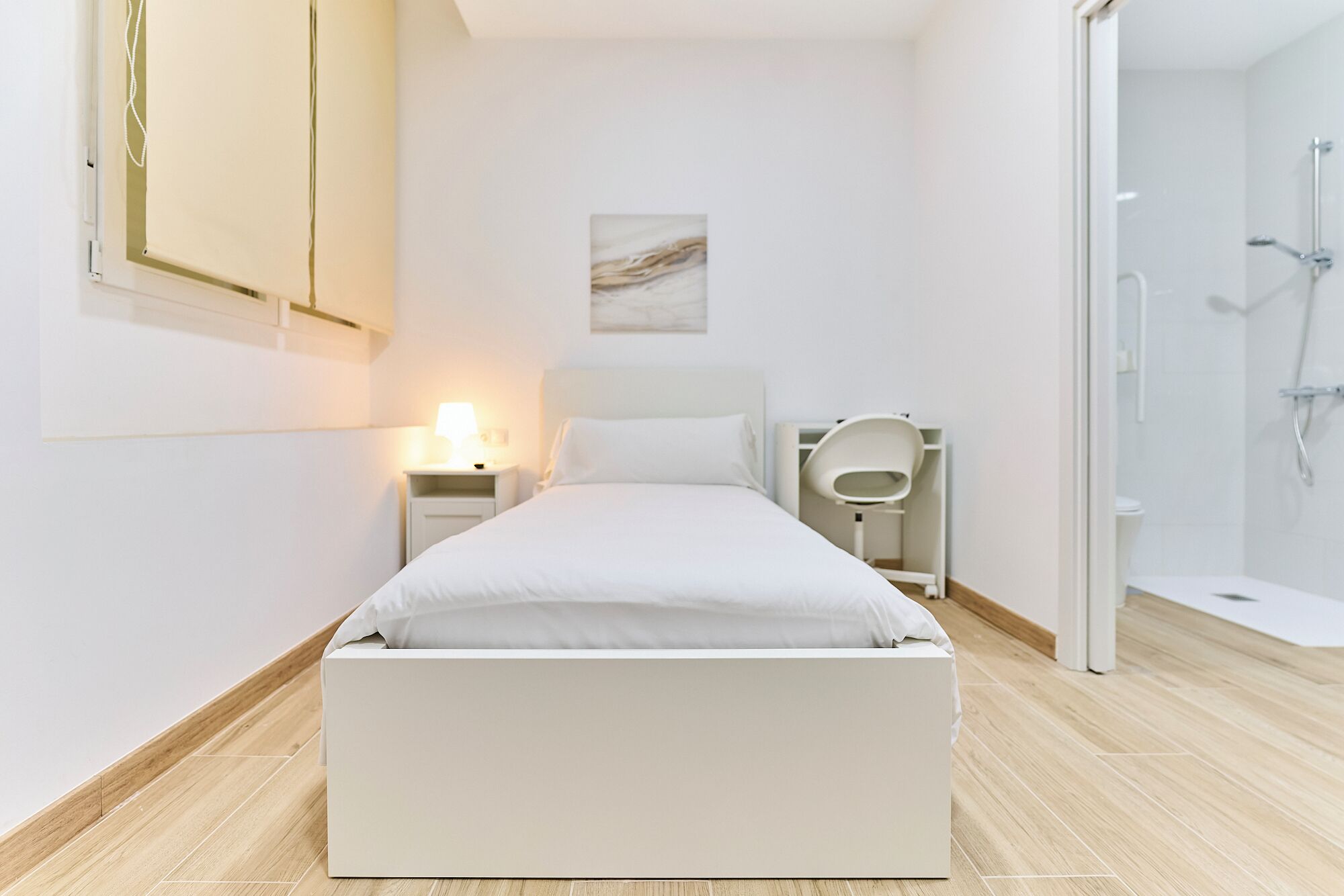 A modern bedroom with a bed, bedside table, lamp, and a shower area.