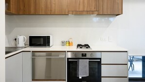 Una cocina moderna con armarios de madera, microondas, hervidor, cocina a gas y lavavajillas.